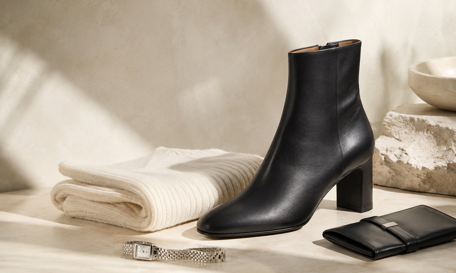 Eternal Things editorial still life with black leather ankle boot, cream knitwear, silver watch and black leather wallet